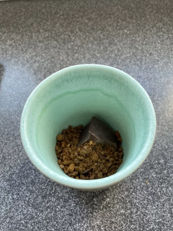 Chunk of ceremonial cacao and panela granules in a handcrafted turquoise ceramic cup, ready for preparation.