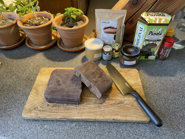 A 1kg Inka Gold ceremonial cacao block split in half on a rustic wooden board, surrounded by natural ingredients like panela and spices.