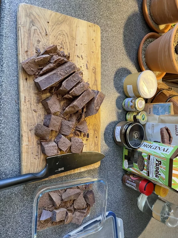 Fourth stage of preparing a 1kg ceremonial cacao block – square chunks being cut on a wooden board with knife and storage container visible.