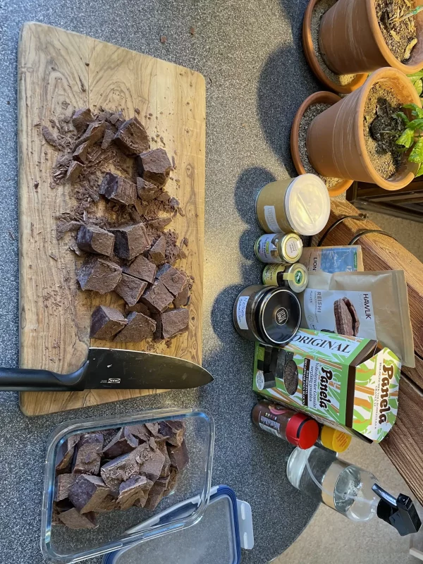 Fifth stage of chunking a 1kg ceremonial cacao block – evenly sized pieces arranged on a cutting board, with most transferred into a glass container.