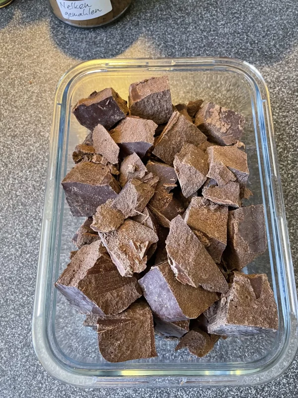 Chunked ceremonial cacao pieces stored in a transparent glass container, ready for daily drink preparation.